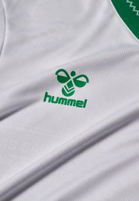 Maglia sportiva bianca con tessuto strutturato, scollo verde e logo stampato verde di un'ape stilizzata con la scritta "hummel".