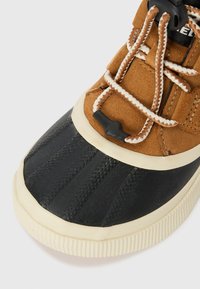 Brown suede upper with black rubber toe cap. White and brown laces, textured rubber outsole, and cream-colored midsole.