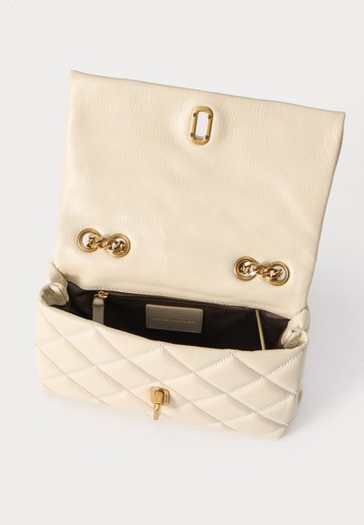 Κρεμ δερμάτινη τσάντα με εκκεντρική ραφή, ανοιχτό καπάκι, χρυσές αλυσίδες στο εσωτερικό καπάκι και ορατή εσωτερική θήκη με φερμουάρ, σε λευκό φόντο.