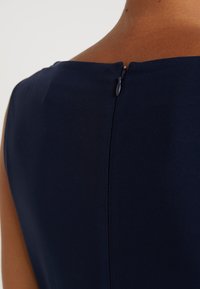 Vestido azul marino con una textura suave, que cuenta con un cierre de cremallera oculto en la parte posterior y un diseño de escote simple y elegante.