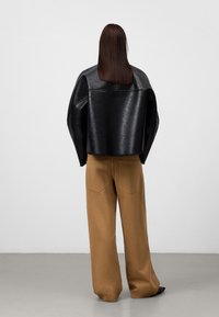 Giacca cropped in finta pelle nera con maniche larghe, abbinata a pantaloni a gamba larga tan a vita alta. Tessuto liscio e design minimalista.