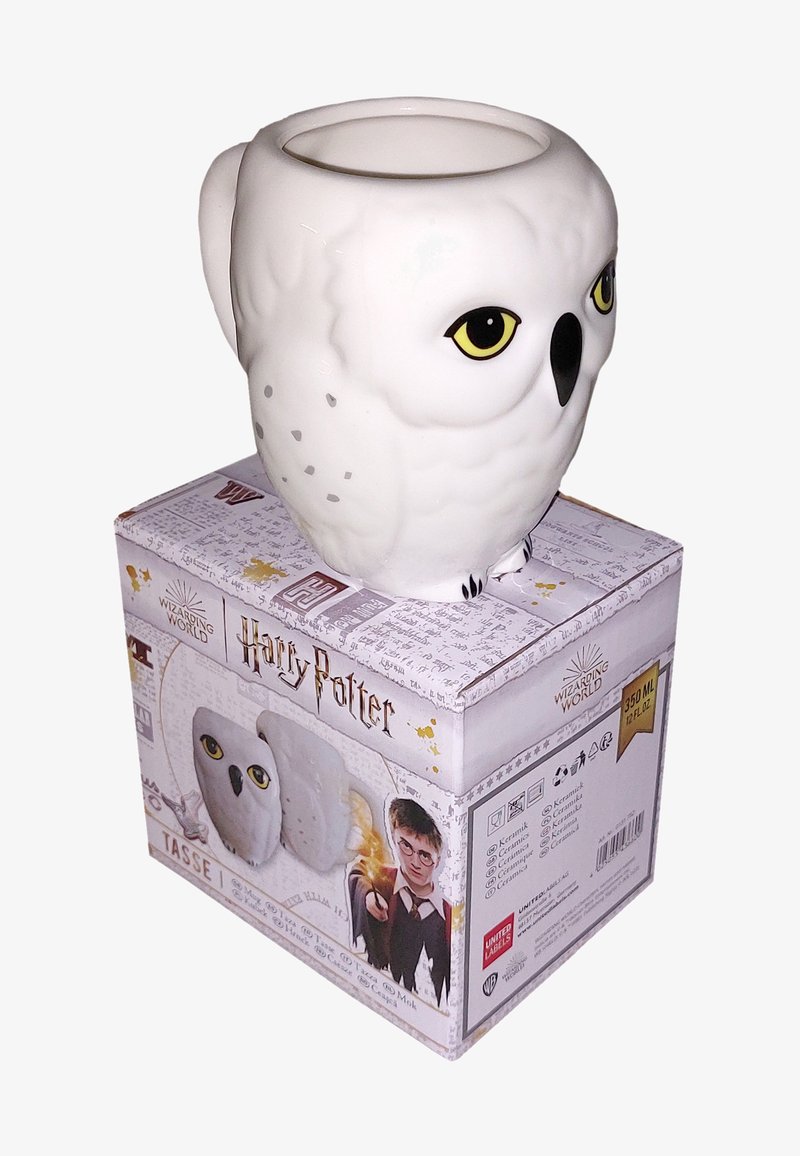 Tazza in ceramica bianca a forma di gufo, con grandi occhi gialli e un corpo texturizzato. La scatola è decorata con il marchio "Harry Potter" e illustrazioni.