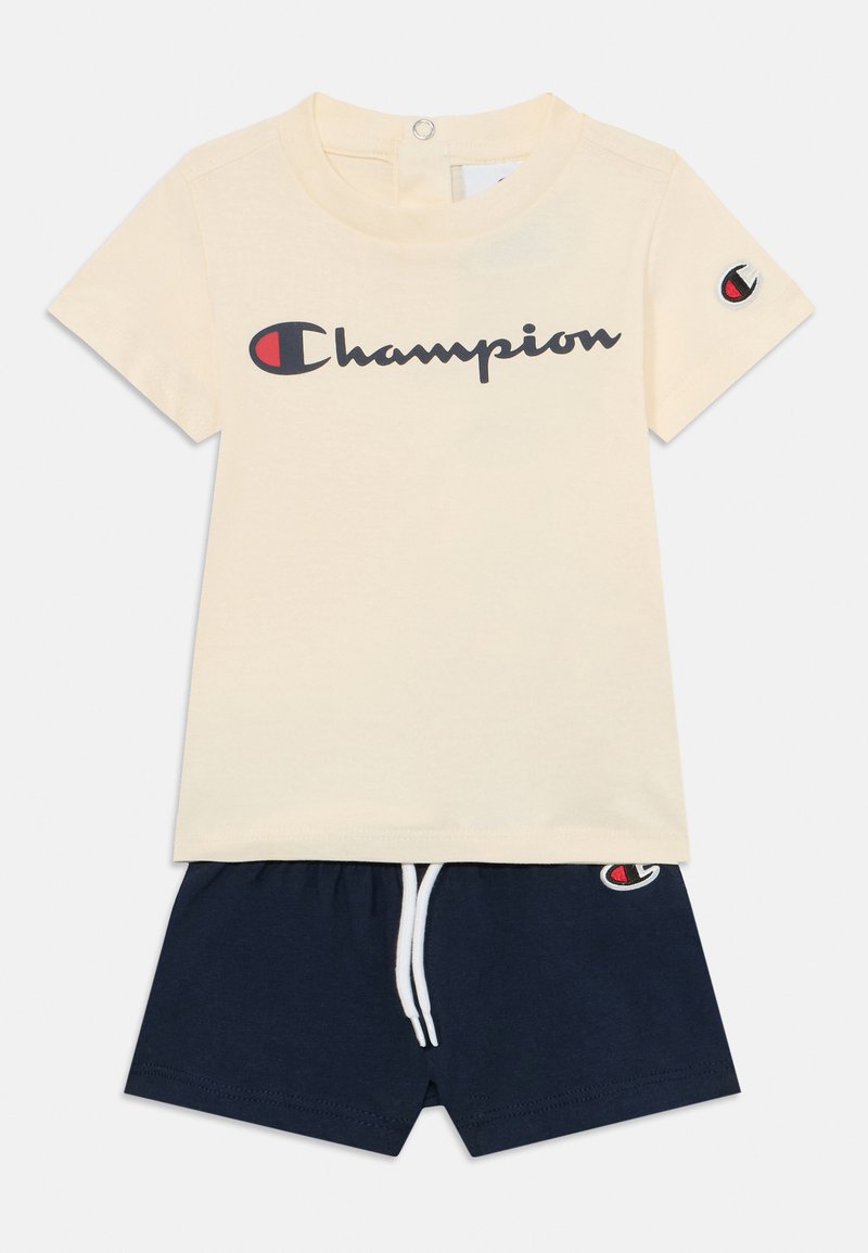 T-shirt cream de manga curta com o logótipo "Champion", combinado com calções azul-marinho com cintura elástica e cordão, logótipo na bainha.
