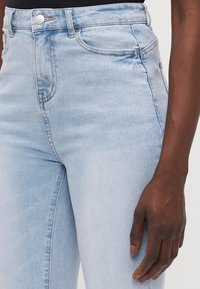 Vaqueros de talle alto en un azul claro con una textura de denim suave, que cuentan con bolsillos frontales, pasadores para cinturón y un cierre de botón plateado.