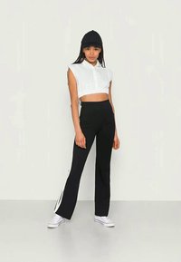 Camisa branca de botão cortada, calças pretas de cintura alta com riscas laterais brancas e boné preto, combinados com sapatilhas brancas.