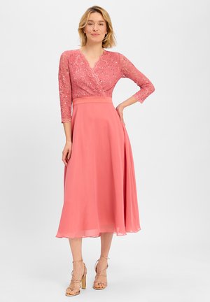 Rosa knielanges Kleid mit einem Spitzen-Oberteil, Dreiviertelärmeln und einem fließenden Chiffonrock. Mit gewelltem Ausschnitt und betontem Taillenbereich.