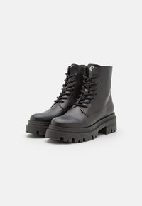 Bottines en cuir noir avec un bout rond, un laçage à l'avant et une semelle en caoutchouc noir épaisse avec des sculptures profondes pour une meilleure traction.