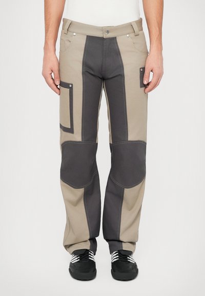 Beige en donkergrijze cargo broek met patchzakken, verstevigde knieën, strakke silhoutte en contrasterende stiksels. Gemaakt van duurzaam katoen.