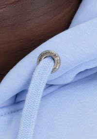 Tela de sudadera de color azul claro con cordón tejido y ojales plateados grabados con "INDUSTRIES USA". Textura suave.