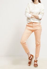 Biała bluza z geometryczną teksturą, zestawiona z jasnoróżowymi chinosami i brązowymi sandałami na platformie z paskami i plecioną podeszwą.