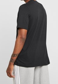 Black cotton t-shirt with short sleeves, a crew neckline, and a relaxed fit. Visible stitching detail along the hem and shoulders.
