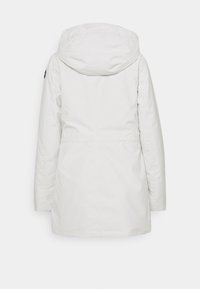 Parka blanche à capuche avec manches longues, texture lisse et taille ajustable. Comprend un emblème noir sur la manche gauche.