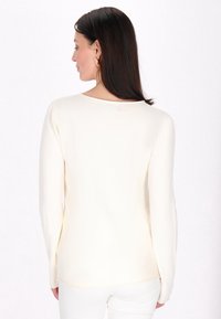 Cremfarbener Langarmshirt mit Rundhalsausschnitt, glatter Textur und lockerer Passform. Der Rücken zeichnet sich durch einfache Nähte und eine leichte Kurve am Saum aus.