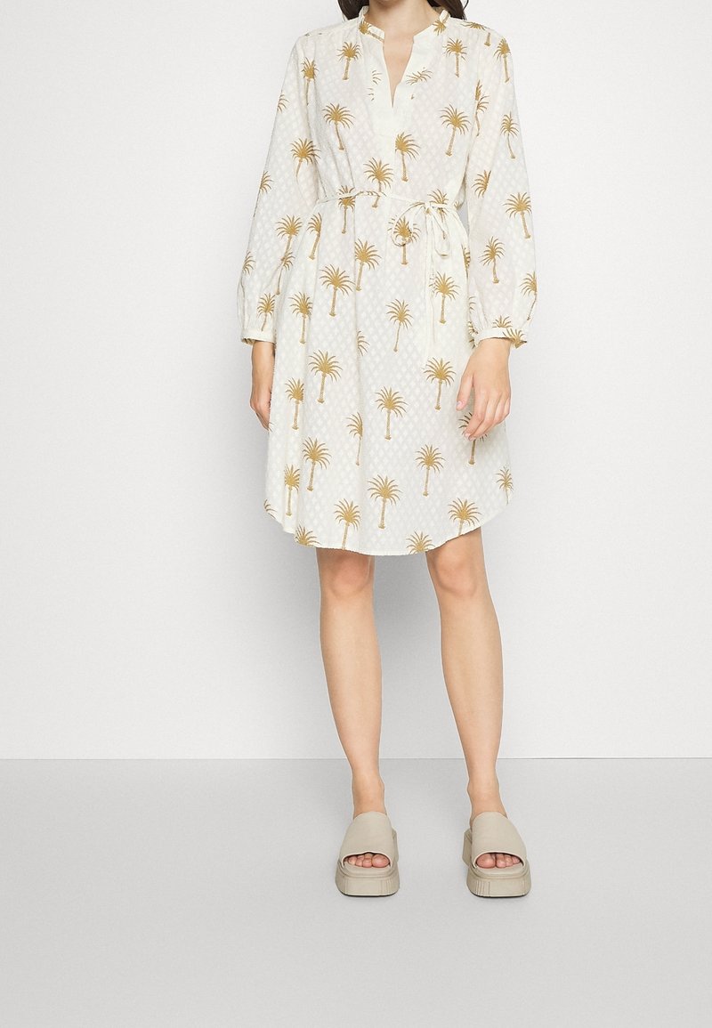 Vestido blanco con patrón de palmeras en dorado, con escote en V y mangas largas, ceñido a la cintura con un cinturón a juego.