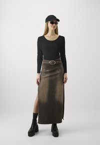 Maglietta nera a coste a maniche lunghe, gonna lunga in denim marrone con apertura frontale, fibbia argentata, stivali platform neri e cappellino nero.