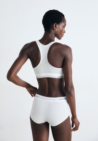 Bijeli pamukasti sportski grudnjak i gaćice s dizajnom racerback. Imaju glatku teksturu i Calvin Klein logotip na elastičnim trakama.