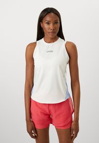 Vit ärmlös träningsstad med blå sidoförstärkningar och logotyp, tillsammans med rosa shorts med en texturerad design och lagerstruktur.