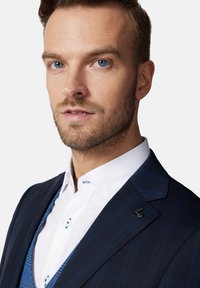 Marynarkę w niebiesko-białe paski z wyraźnym klapem zestawiono z białą koszulą z niebieskimi akcentami oraz kontrastową niebieską kamizelką pod spodem.