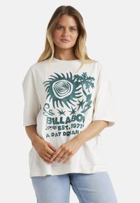 Kortærmet, oversized hvid t-shirt med teal grafik, der har teksten "BILLABONG EST. 1973 A DAY DREAM" samt abstrakte designelementer.