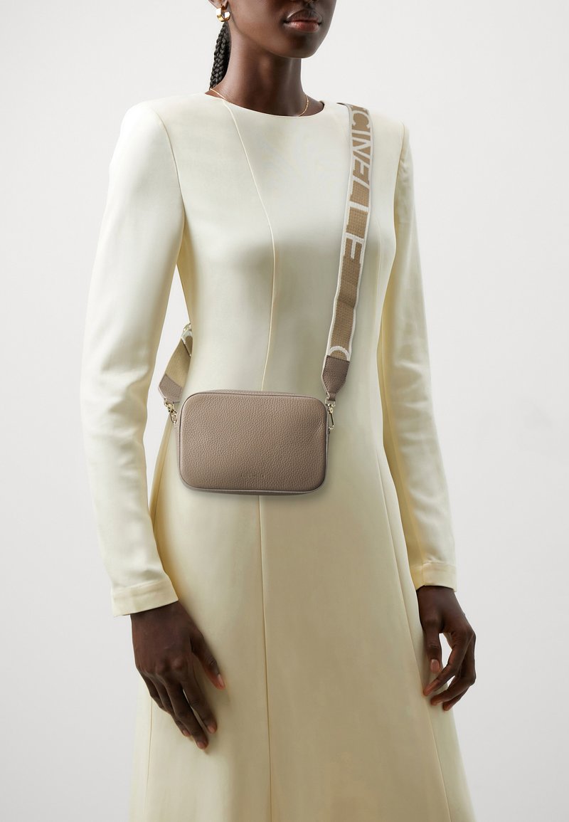 Sac bandoulière en cuir marron avec une finition texturée, doté d'une sangle beige avec logo imprimé. Forme rectangulaire et design minimaliste.