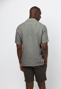 Korte mouwen, lichtgrijs linnen shirt met een relaxte pasvorm en platte kraag, gecombineerd met donkere shorts. Subtiele textuur en een schoon ontwerp.