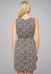 Robe florale avec une taille cintrée, présentant un fond noir, des fleurs roses et blanches, et un design sans manches. Le dos révèle un décolleté en V.
