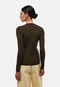 Chemise à manches longues côtelée vert olive avec un design ajusté et un col rond, portée avec un pantalon large de couleur claire.