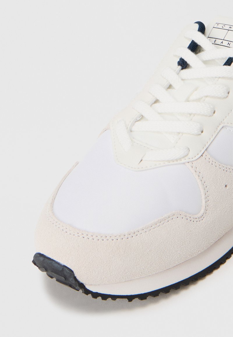 Light-colored sneaker featuring a mix of suede and mesh materials, white and beige tones, rounded toe, and textured rubber sole.