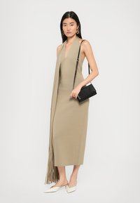Beige, sleeveless dress with a V-neck and fringed detail at the hem. Paired with a black crossbody bag and white pointed-toe flats.