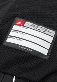 Black mesh fabric featuring a label with a red logo, fields for names, and the text "HAND ME DOWN" at the bottom.