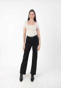 Top beige ajustado de escote cuadrado, vaqueros negros de tiro alto acampanados, botines negros de punta con tejido suave y costuras sutiles.