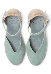 Zelené semišové espadrilky s tkaninou béžové barvy na svršku, nastavitelným páskem kolem kotníku a texturovanou modrou stélkou. Design špičky ve tvaru V.