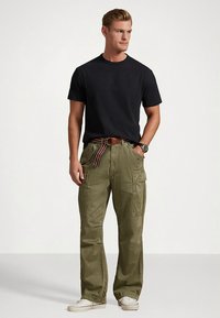 Μαύρο κοντομάνικο μπλουζάκι συνδυασμένο με χακί παντελόνι καμπαρντίνα με πλαϊνές τσέπες. Μια ριγέ ζώνη προσθέτει λεπτομέρεια, που συνδυάζεται με λευκά αθλητικά παπούτσια.