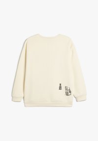 Sudadera color crema con un ajuste holgado, cuello redondo e ilustraciones impresas de dos perros en la parte baja de la espalda. Textura suave y puños acanalados.