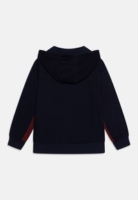 Sweatshirt bleu marine avec capuche et manches côtelées, présentant des accents rouges sur les côtés. Tissu doux avec une texture lisse.