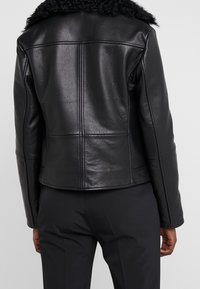 Giubbotto in pelle nera con colletto texturizzato, design cropped e dettagli di cuciture visibili. Superficie liscia, silhouette aderente e linee pulite.