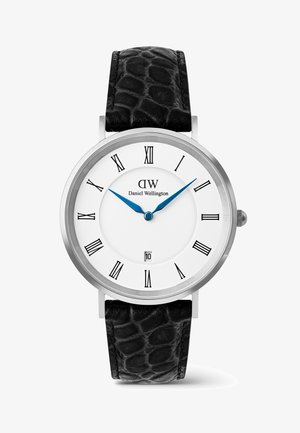 Montre ronde en argent avec cadran blanc, chiffres romains noirs, aiguilles bleues indiquant 10h08, bracelet en cuir noir texturé et affichage de la date à 6 heures.