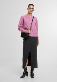 Rosa Langarmpullover mit geripptem Saum, kombiniert mit einem knielangen schwarzen Jeansrock mit einem Schlitz vorne, und schwarzen Knöchelschuhen. Kleine schwarze Tasche.