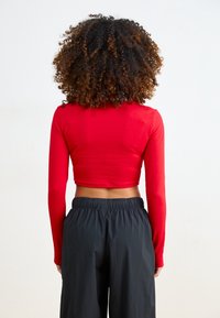 Röd långärmad crop top med en figurnära design och slät textur, kombinerad med svarta högmidjade byxor med elastisk midja.