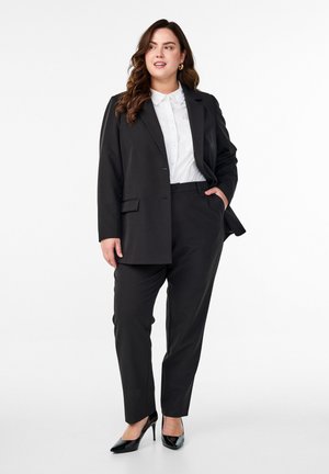 Black tailored suit featuring a single-button blazer, fitted trousers, and a white button-up shirt, paired with black high heels.
