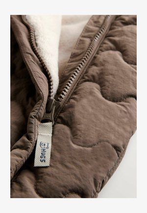 Hnědá prošívaná bunda s měkkou krémovou podšívkou, vybavená zipem YKK a světle modrou nálepkou s embosovaným nápisem "HUGS".