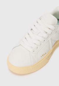 White sneaker featuring a smooth leather upper, round toe, textured cream midsole, and contrasting mint green lining with logo detail.