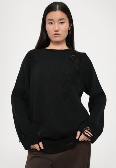 Black oversized sweater with intricate floral embroidery, distressed detailing, and a textured knit. Features long sleeves and ribbed cuffs.
