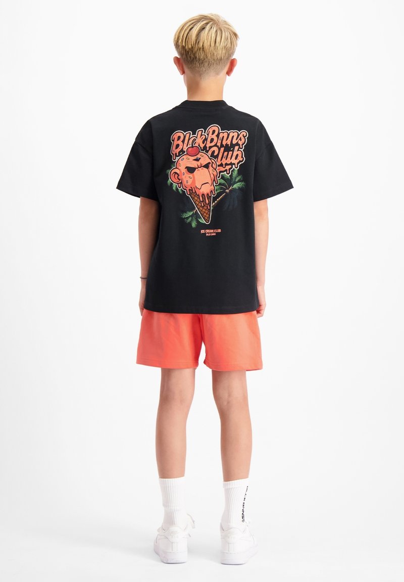 Zwarte short-sleeve t-shirt met een kleurrijke ijscremgraphics en tekst op de achterkant, in combinatie met oranje shorts en witte sneakers.
