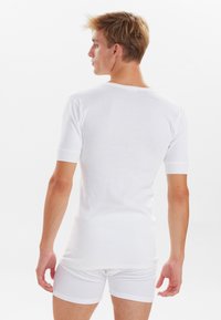 Hvid bomulds t-shirt med korte ærmer og rund halsudskæring, båret med matchende hvide boxershorts. Glat tekstur, enkelt design.