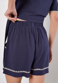Shorts blu navy, con texture, dotati di una cintura elastica e di un bordo decorativo color crema lungo l'orlo e le tasche.