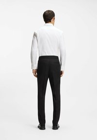 Schwarze Hose mit lockerem Schnitt und elastischem Taillenbund, kombiniert mit einem weißen Langarmhemd. Glatter Stoff und klares Design.