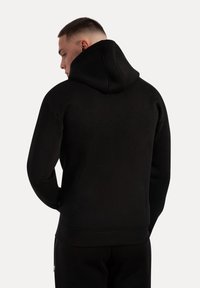 Sudadera negra con superficie texturizada y bolsillo canguro, con una capucha profunda y dobladillos y puños de canalé, vista desde atrás.