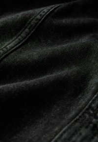 Zwarte denimstof met een gladde textuur, voorzien van subtiele horizontale lijnen, gevouwen randen en een zachte glans.