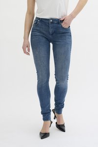 Temno modri skinny kavbojki s klasičnim pet-džepnim dizajnom, ki vključuje diskretno bledenje, dopolnjeni s črnimi čevlji na visoki peti z ostrim nosom.